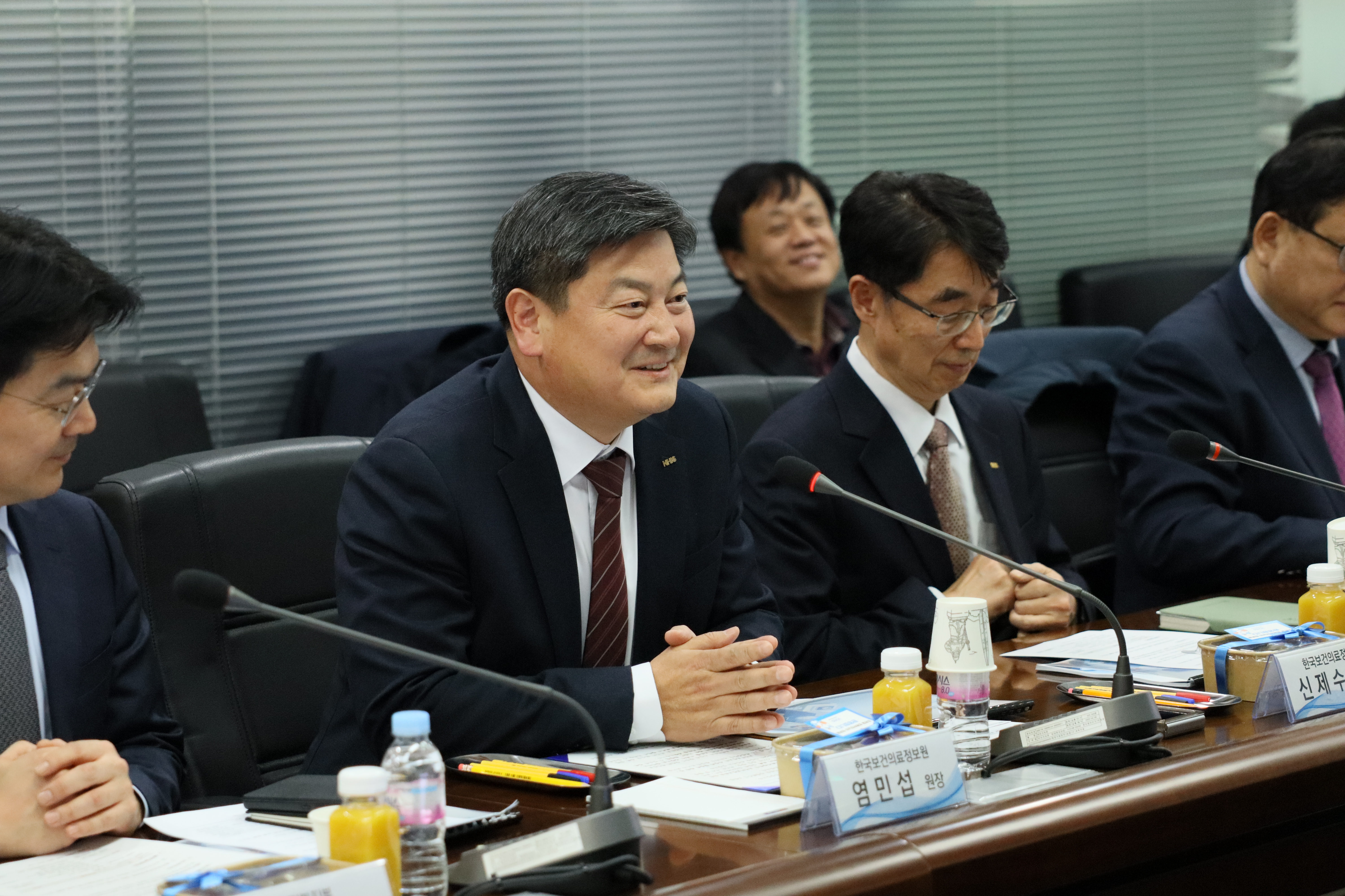 회의 테이블에 앉아 있는 관계자들이
마이크와 자료를 앞에 두고 진지하게 의견을 나누는 모습이 담겨 있다.

참석자들은 정장 차림으로 회의에 집중하고 있으며,
보건의료데이터 활용과 디지털 헬스케어 정책에 대한
현장의 의견을 공유하는 공식 회의 장면임을 보여준다.

테이블 위에는 회의 자료, 음료, 명패, 마이크 등이 정리되어 있다.
