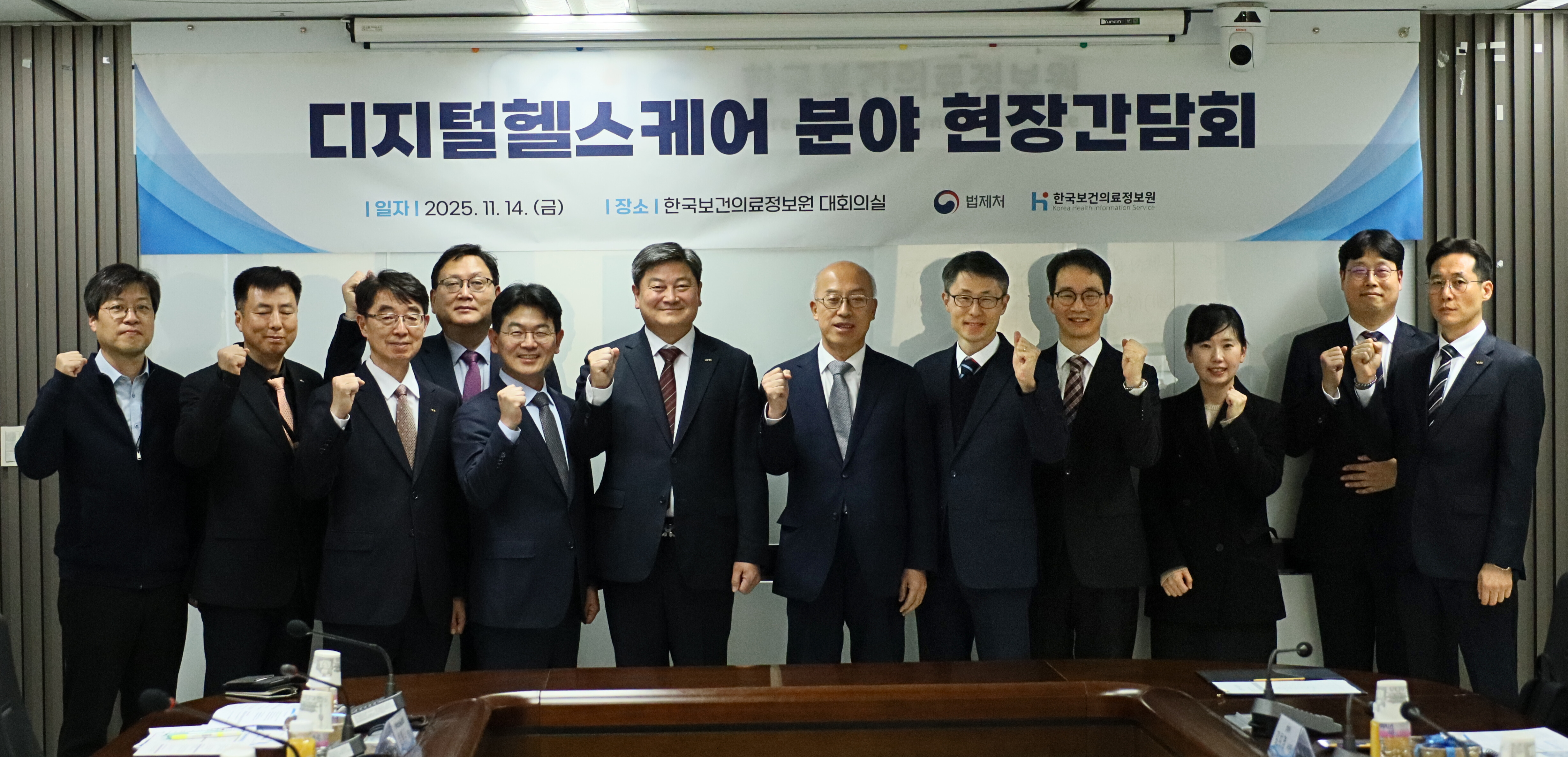 회의실 전면에 설치된 현수막을 배경으로
참석자 전원이 일렬로 서서 주먹을 쥔 포즈로 기념 촬영을 하고 있는 모습이 담겨 있다.
현수막에는 ‘디지털헬스케어 분야 현장간담회’라는 문구와 함께
개최 일시(2025년 11월 14일), 장소(한국보건의료정보원 대회의실),
법제처 및 한국보건의료정보원 로고가 표시되어 있다.

참석자들은 법제처, 보건복지부, 한국보건의료정보원 관계자로 구성되어 있으며,
디지털 헬스케어 및 보건의료데이터 활용과 관련한
현장의 목소리를 제도와 법으로 연결하기 위한
기관 간 협력 의지를 상징적으로 표현하고 있다.
