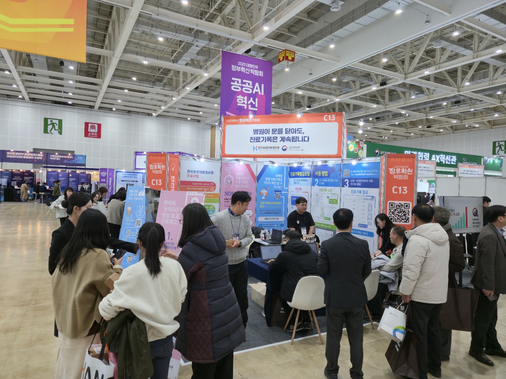 정부혁신박람회 전시장 내 한국보건의료정보원 홍보 부스 전경으로, ‘병원이 문을 닫아도 진료기록은 계속됩니다’라는 문구가 상단에 게시되어 있다. 부스에서는 의료데이터 활용 서비스 안내 패널과 화면을 중심으로 관계자들이 방문객에게 설명을 제공하고 있으며, 여러 관람객이 부스를 둘러싸고 설명을 듣거나 자료를 살펴보고 있다. 전시장 내부에는 ‘공공 AI 혁신’ 등 정부혁신 관련 다른 전시 부스와 안내 배너가 함께 배치되어 있어 행사 분위기를 보여준다.