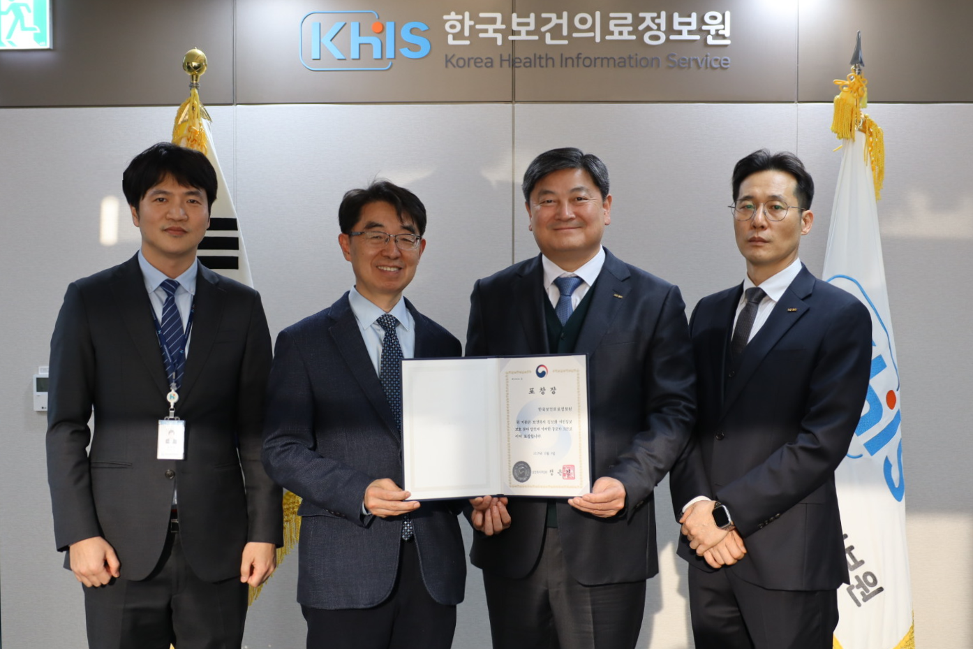 한국보건의료정보원(KHIS) 기관 로고가 보이는 회의실 배경 앞에서 관계자 4명이 정장을 입고 나란히 서서 기념촬영을 하고 있다. 중앙에 선 두 사람이 보건복지부 명의의 표창장을 함께 들고 있으며, 나머지 관계자들도 함께 자리해 공식 수상 행사의 분위기를 보여준다. 해당 사진은 한국보건의료정보원이 개인정보관리 전문기관 지정 등 개인정보 보호 수준 향상에 기여한 공로로 보건복지부 주관 ‘개인정보보호 분야 정보화 유공 표창’을 수상했음을 나타낸다.